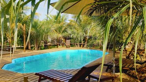 Eine Holzterrasse mit Pool, umgeben von Palmen und Holzliegen.