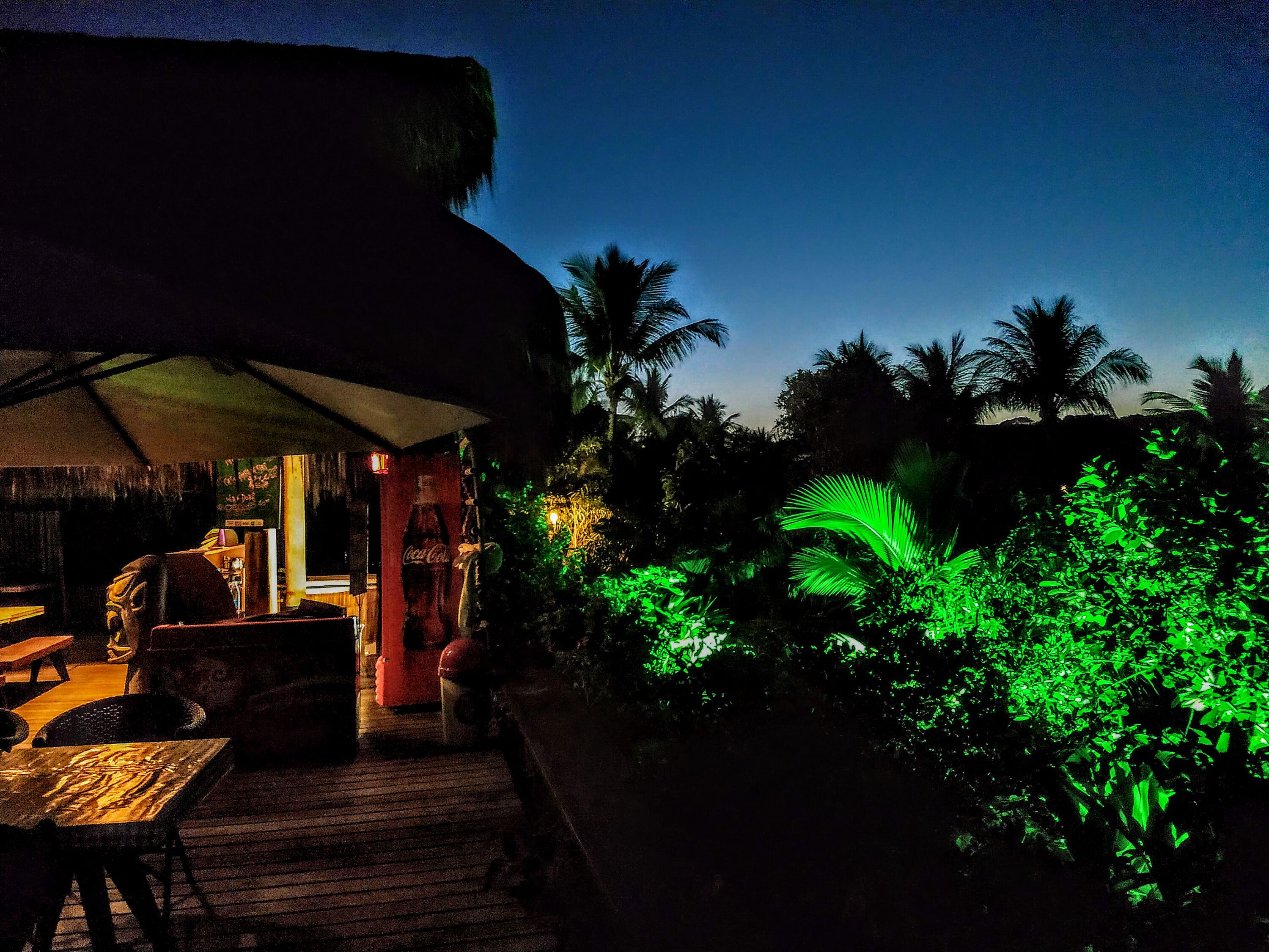 An outdoor seating area with a thatched roof, wooden tables, and chairs.