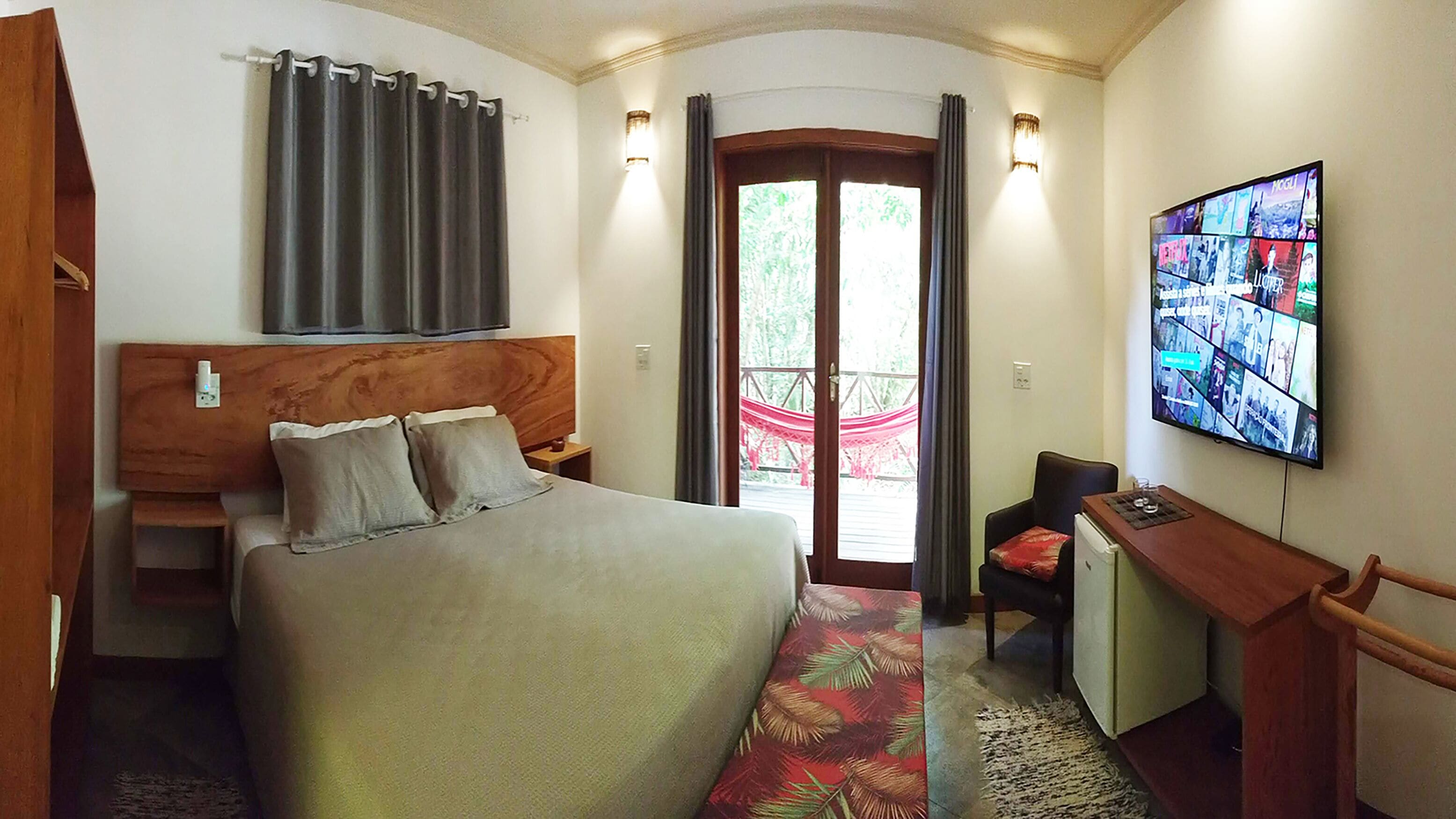 A hotel room with a bed, a desk, a television, and a view of the outdoors.