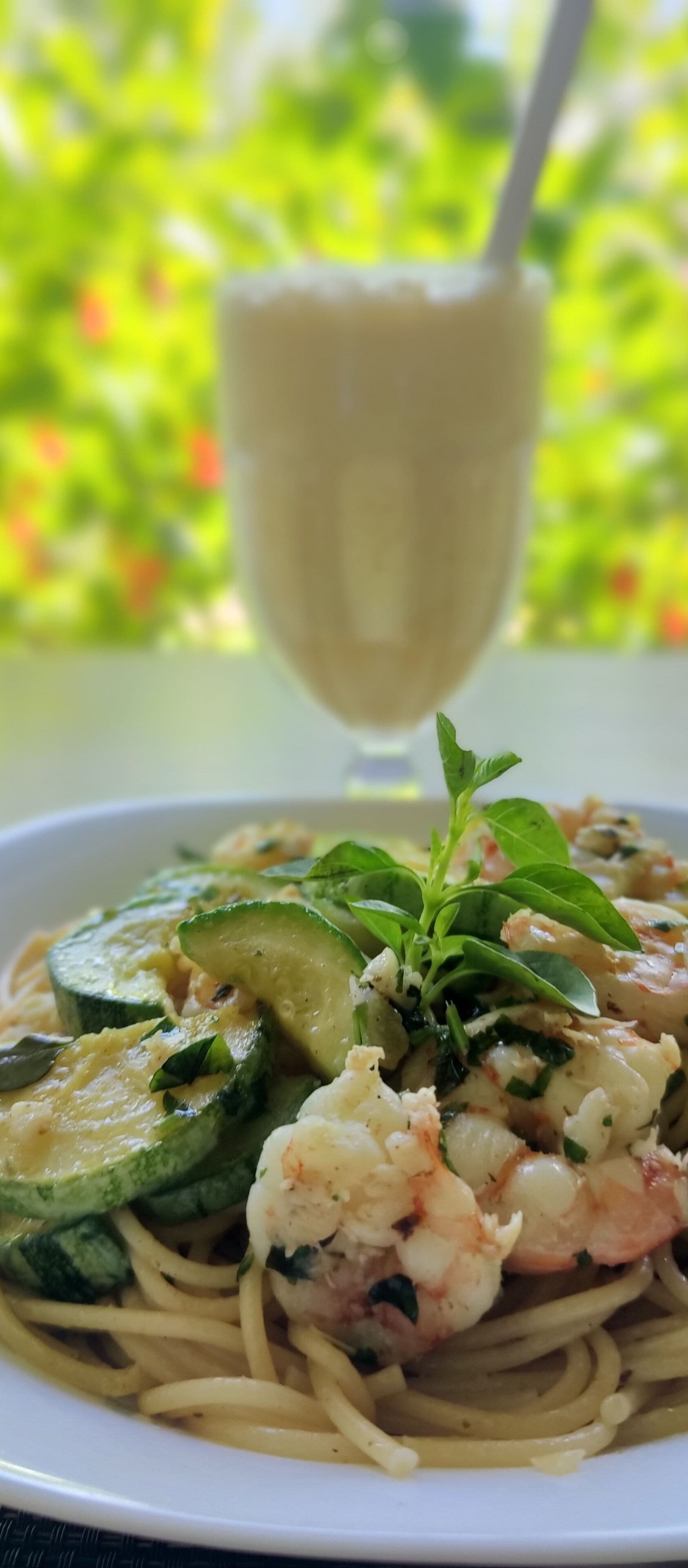 Ein Teller Pasta mit Garnelen und Zucchini, garniert mit Kräutern, sowie ein Glas weißes Getränk.