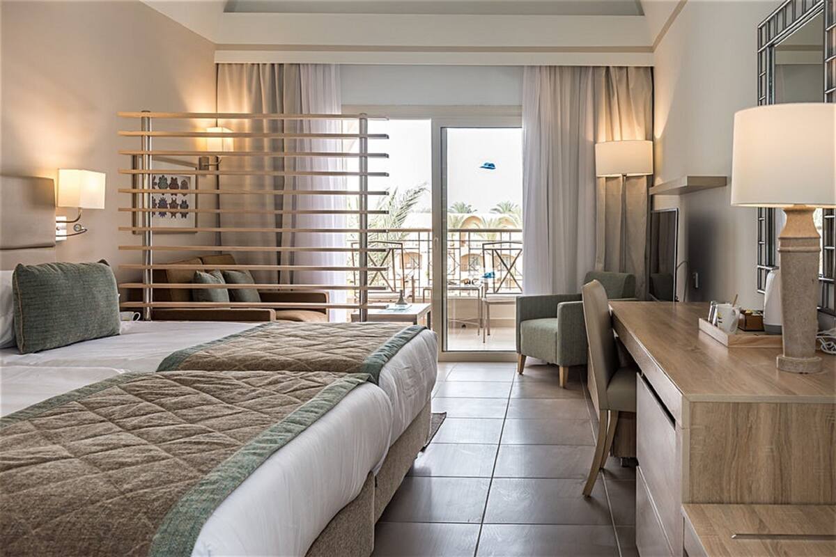 Ein Hotelzimmer mit einem großen Bett, einem Schreibtisch, einem Sessel, einem Balkon mit Blick und einem Fernseher.