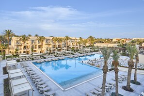 A large swimming pool surrounded by lounge chairs and palm trees, with a hotel building in the background. - Jaz Makadi Gardens - TUI BLUE Makadi Gardens - Adults Friendly 16 Years Plus (Makadi Bay)