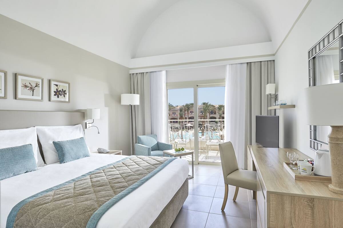 Ein Hotelzimmer mit Bett, Schreibtisch, Stuhl, Fernseher und Blick auf einen Pool und Gebäude.