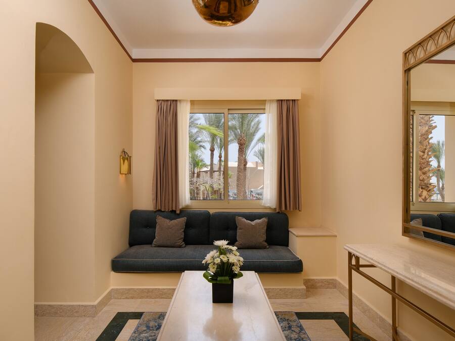 Una habitación con sofá, una mesita de centro con flores, un espejo y una ventana con cortinas.