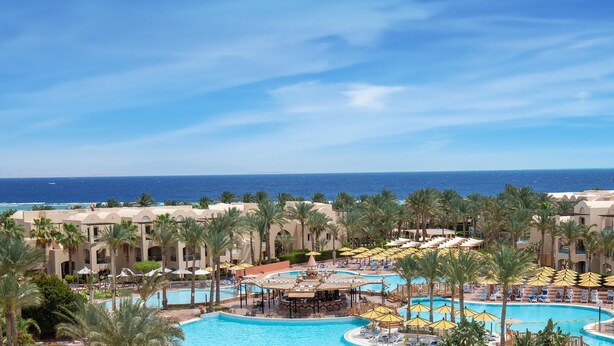 Un resort con una piscina grande, palmeras y vistas al océano.