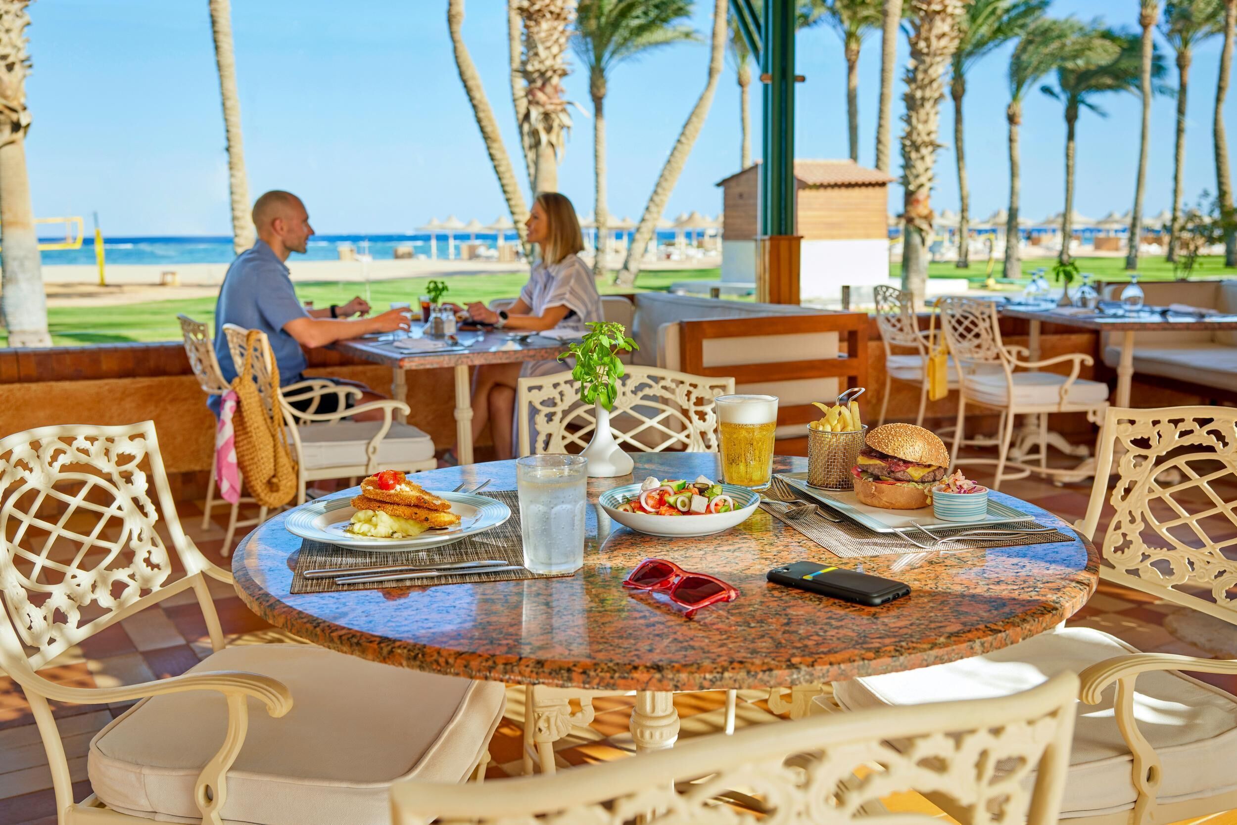 Un espace de restauration en plein air avec vue sur la plage, des tables et des chaises, et une grande variété de plats et de boissons.