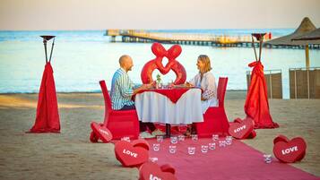 A couple dining at a beachside table with a view of the ocean and pier.