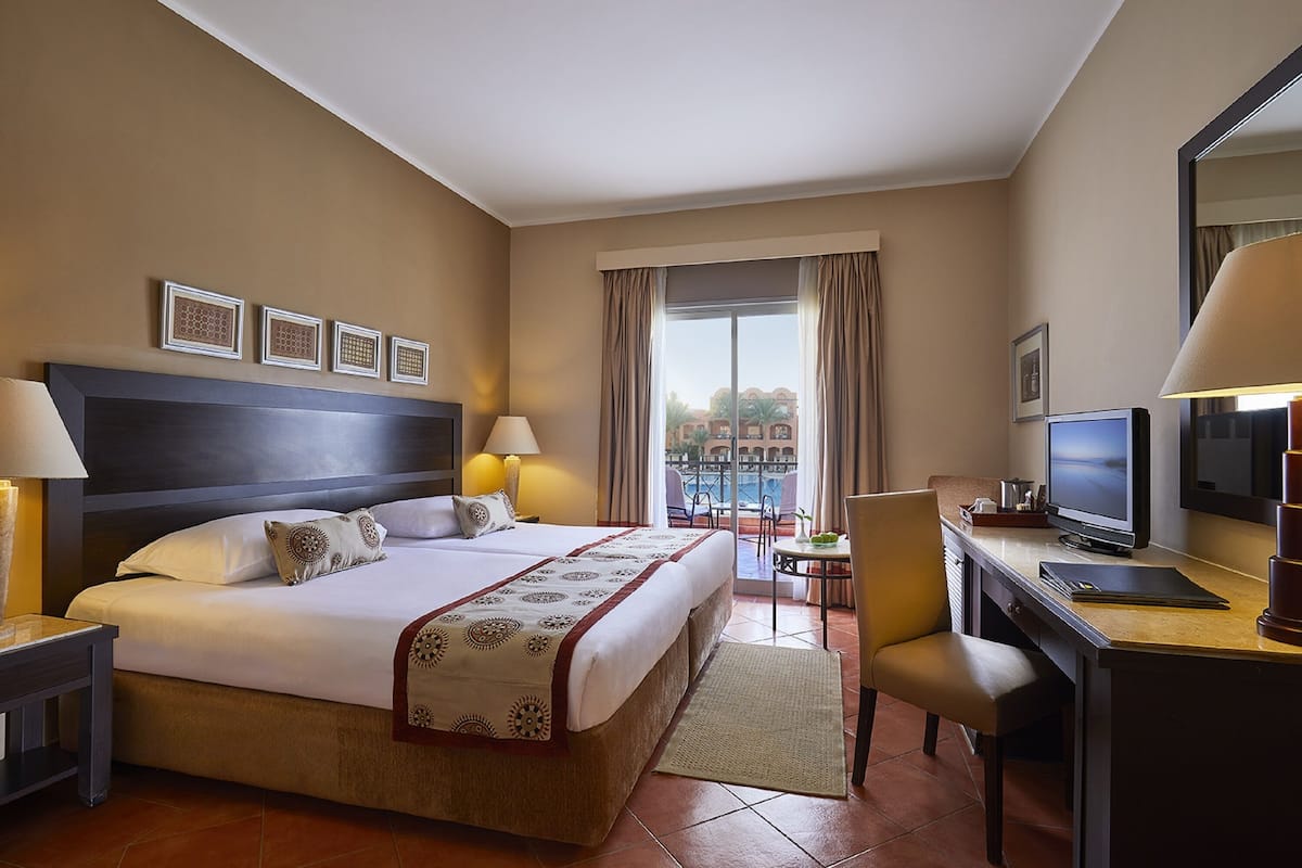 A hotel room with a large bed, a desk with a computer, a chair, and a view of a pool.