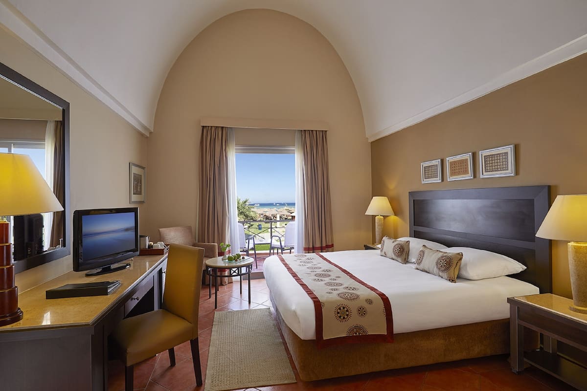 A hotel room with a bed, desk, TV, and a view of the outdoors.