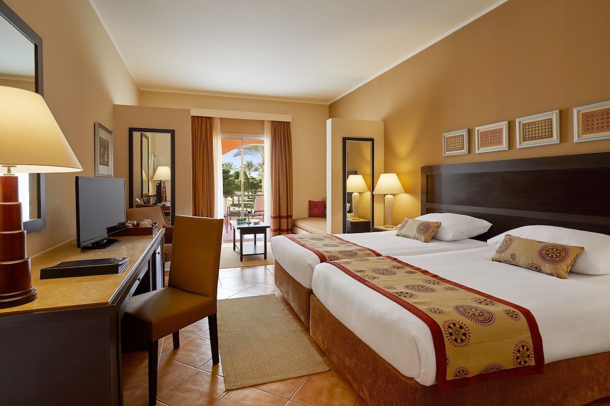 A hotel room with a bed, a desk with a computer, a chair, a TV, and a view of the outdoors.