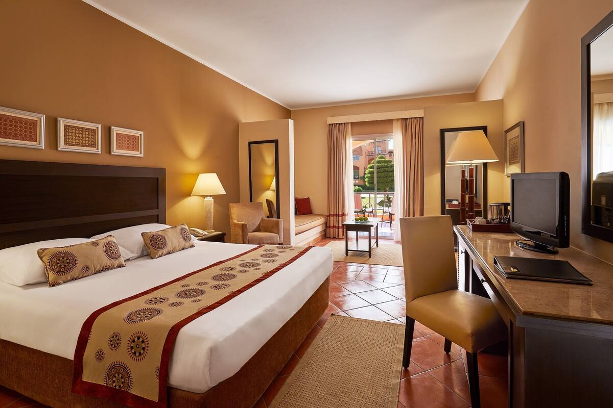 A hotel room with a large bed, a desk with a television, and a view of the outdoors.