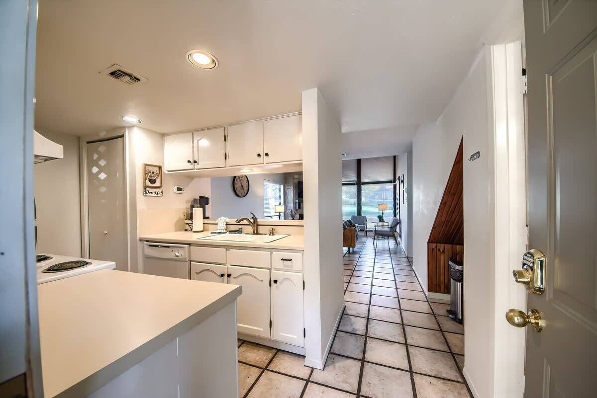 A kitchen with white cabinets, a sink, and a stove. There is a dining area with a table and chairs visible in the background.