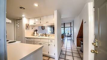 A kitchen with white cabinets, a sink, and a stove. There is a dining area with a table and chairs visible in the background.