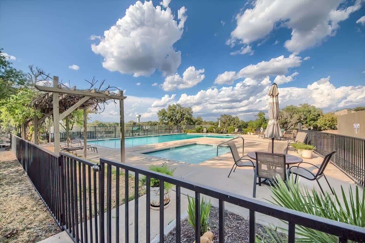 A swimming pool with lounge chairs and umbrellas, surrounded by a fence and greenery.