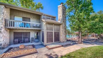 A two-story house with a stone chimney, a balcony, and a pool in the background.