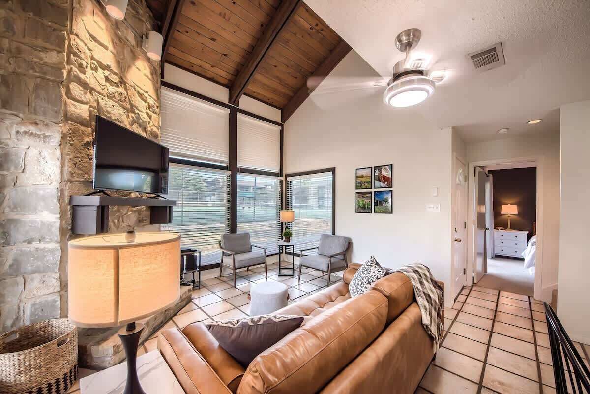 A living room with a stone wall, a fireplace, a sofa, a TV, and a ceiling fan.