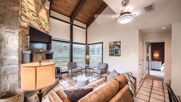 A living room with a stone wall, a fireplace, a sofa, a TV, and a ceiling fan.
