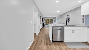 A modern kitchen with white cabinetry, a stainless steel dishwasher, and a wooden floor. - TB 9G Great dog friendly 2 bedroom condo on the golf course at True Blue 9G (Pawleys Island)