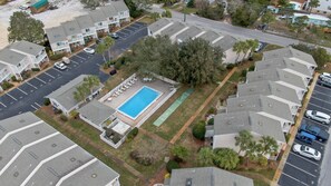 Vista aèria d'una zona residencial amb piscina, un pati tancat per una tanca, diverses places d'aparcament i cases de diferents estils de teulada.