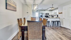 A dining area with a long table and woven chairs, a kitchen in the background, and a door labeled "Bungalow". - Emerald Escapes unit 41 (Miramar Beach)