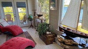 A cozy room with a large window, a wooden ship model, a globe, and a red cushioned bench.