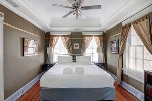 A hotel room with a large bed, two bedside tables, a ceiling fan, and a window with curtains. - York Street Gem - A Taste of 1800s Savannah (Savannah)