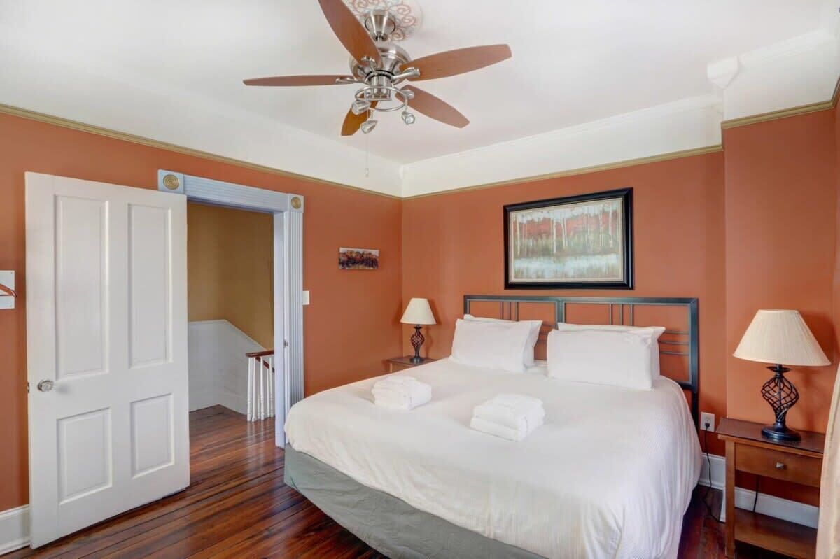 Une chambre d’hôtel avec un lit, deux tables de chevet, un ventilateur de plafond et une porte donnant sur une autre pièce.