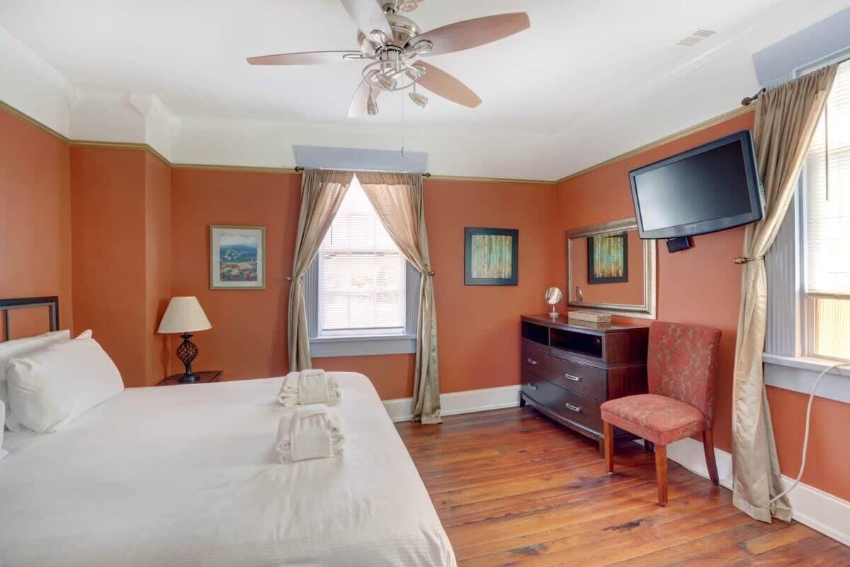 Une chambre d’hôtel équipée d’un lit, d’un bureau, d’une chaise, d’une télévision et d’un ventilateur de plafond.