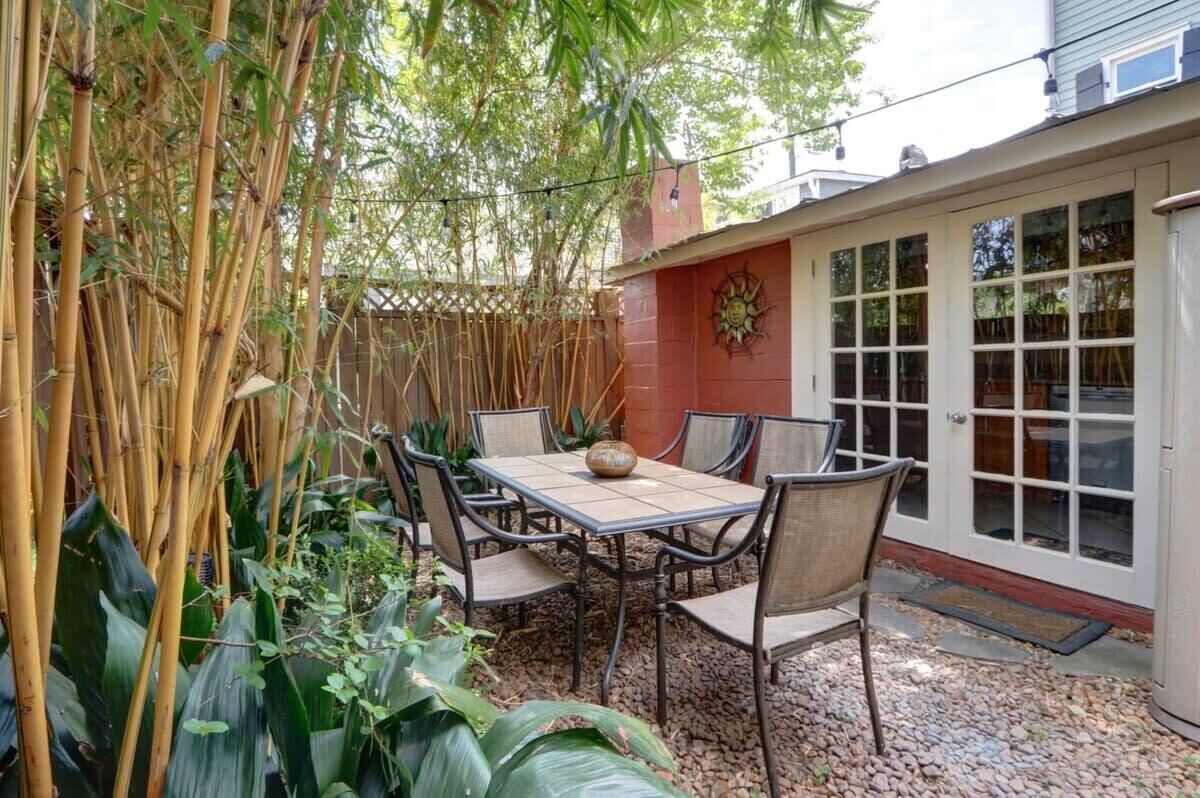 A patio with a table and chairs, surrounded by bamboo plants and a red wall with a decorative sun motif.