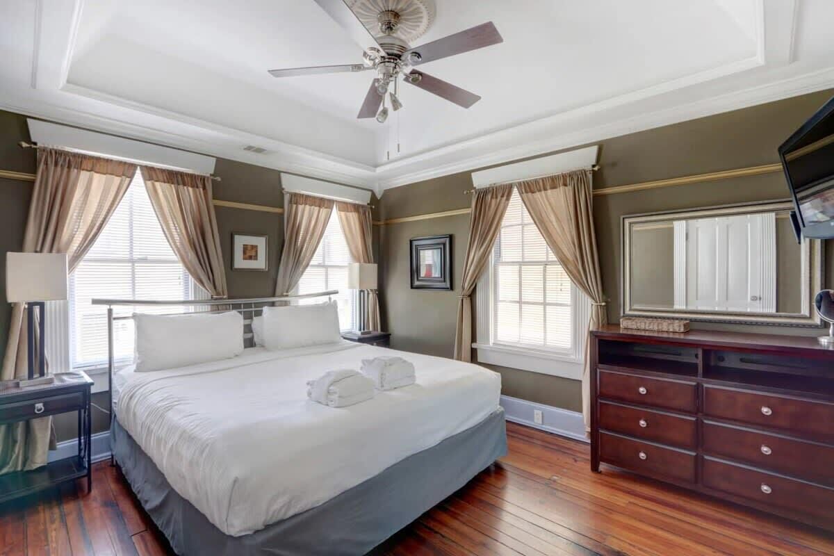 Habitación de hotel con una cama grande, ventilador de techo, cómoda y una ventana con cortinas.