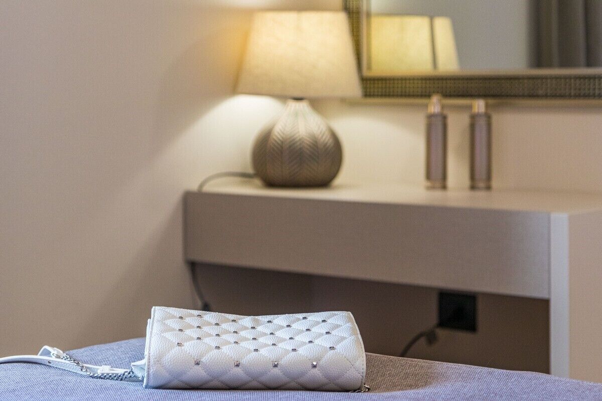 Une chambre d’hôtel bien rangée, avec une table de chevet, une lampe et un petit sac à main blanc posé sur le lit.