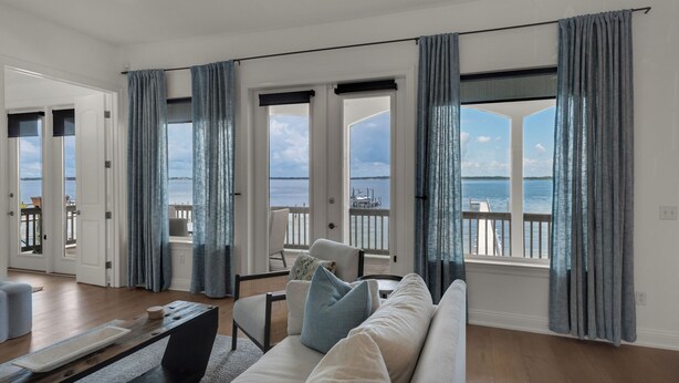 A spacious living room with a large window overlooking a marina, a sofa with cushions, and a wooden coffee table. - 🌅 Let's Do Sunset - Dock, Gulf Access, Sunset Deck + Pet Friendly 🐾 (Pensacola Beach)