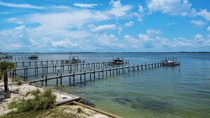 A marina with multiple docks extending into calm waters, surrounded by clear skies and distant land. - 🌅 Let's Do Sunset - Dock, Gulf Access, Sunset Deck + Pet Friendly 🐾 (Pensacola Beach)