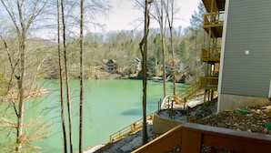 Blick auf einen See mit einer Holzterrasse und Treppen, die zu einem Gebäude mit Balkonen führen.