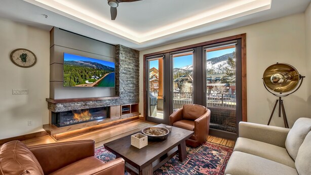 Ein modernes Wohnzimmer mit Kamin, Ledersofas, Fernseher und einem großen Fenster mit Blick auf die Berge.