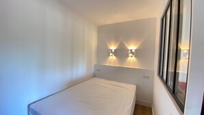 Une petite pièce, bien aménagée, avec un lit simple, deux lampes fixées au mur et une fenêtre sur le côté droit.