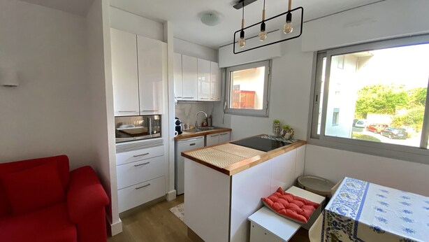 Une cuisine compacte avec des meubles blancs, un four à micro-ondes, un évier et une fenêtre donnant sur la rue.