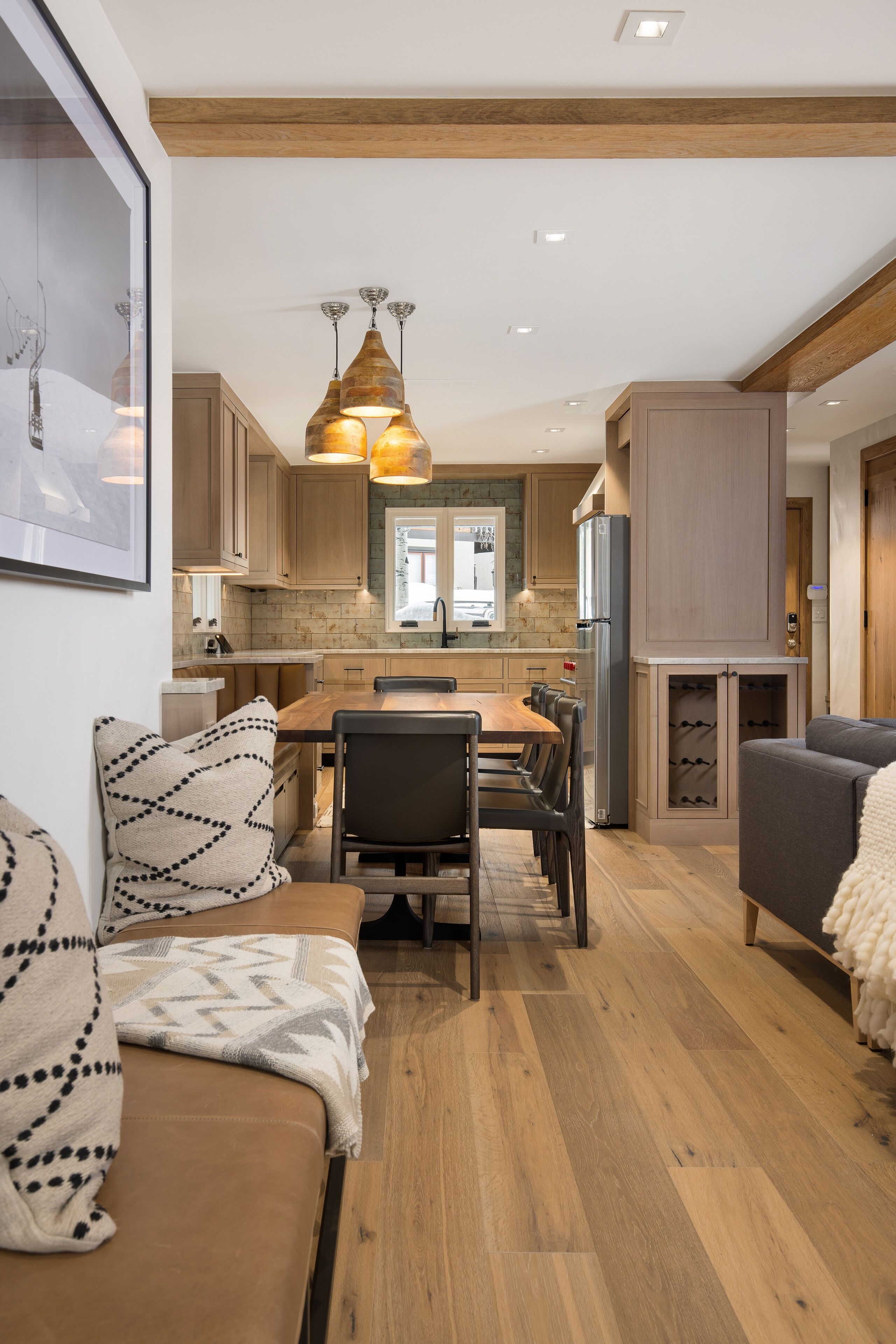 A modern kitchen with wooden cabinets, a dining area with a table and chairs, and a cozy seating area with a sofa and cushions.