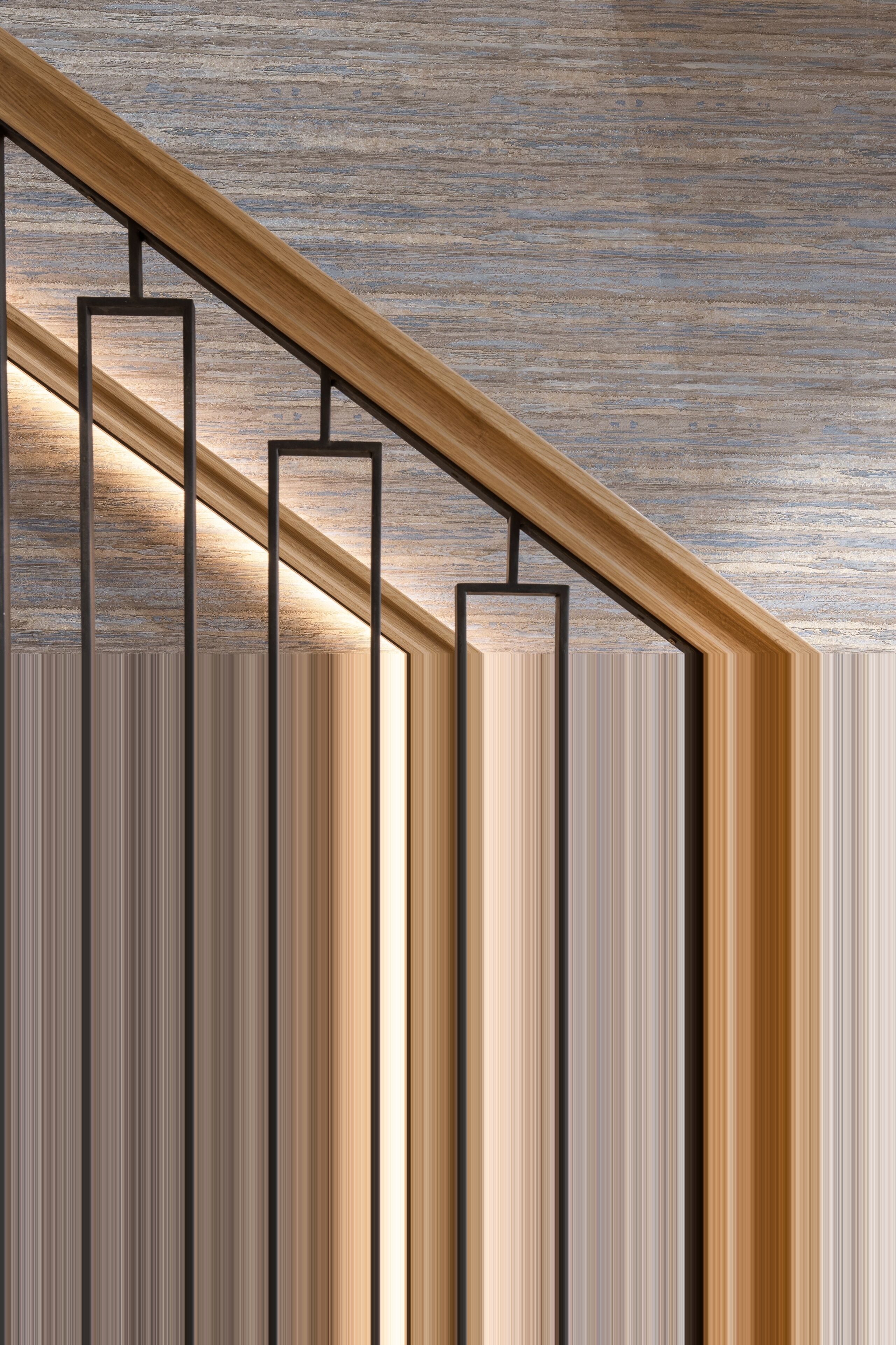 A wooden staircase with black metal railings against a textured wall.