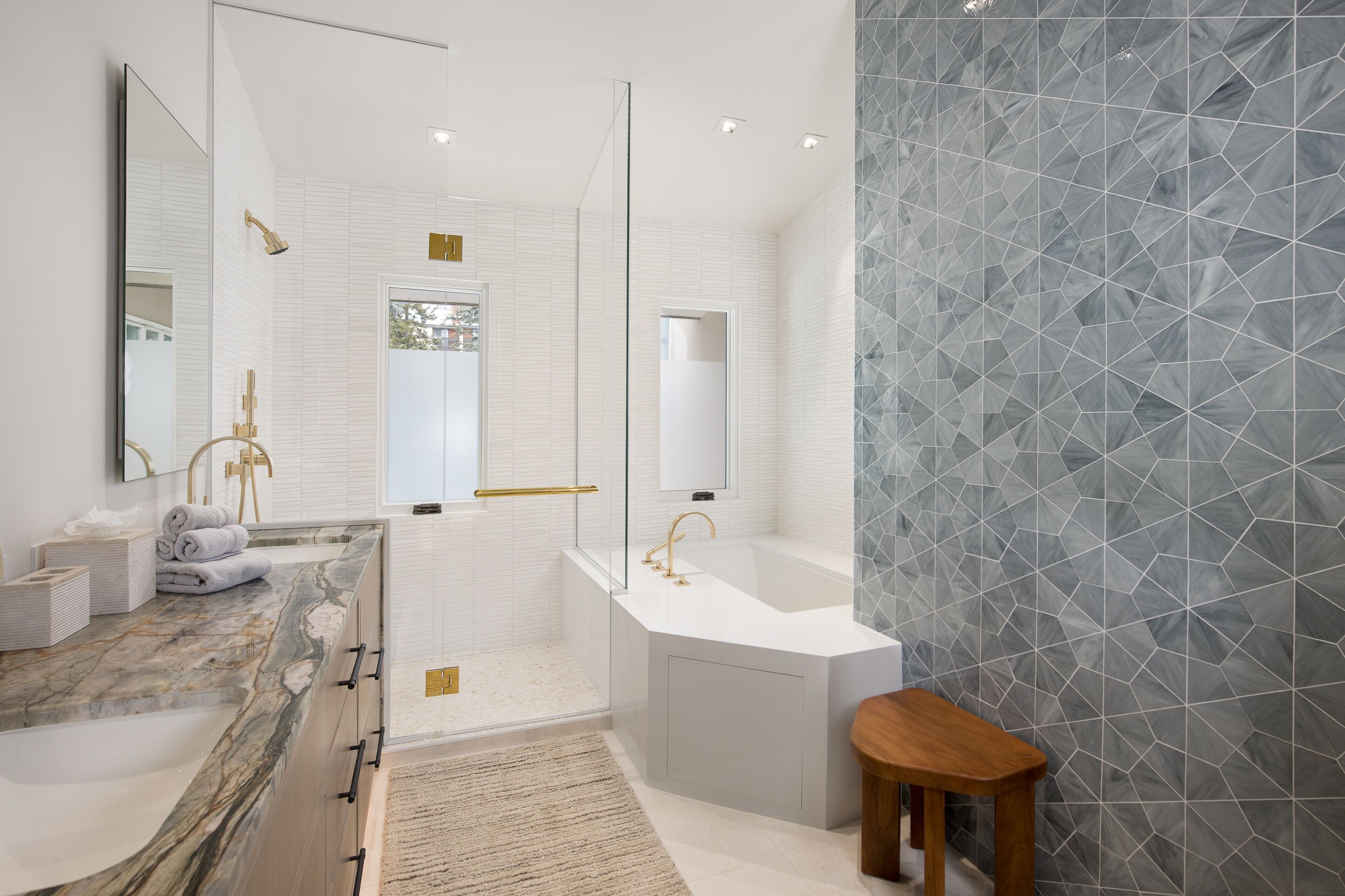 Een moderne badkamer met een marmeren aanrechtblad, een vrijstaand bad en een wand met een geometrisch patroon.