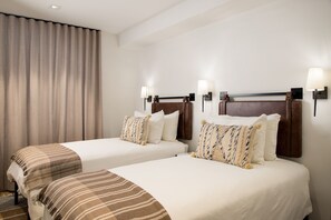 A hotel room with two beds, each with a headboard, white bedding, and decorative pillows. There are wall-mounted lamps on either side of the beds. - Vail Trails East #10a 3 Bedroom Condo by RedAwning (Vail)