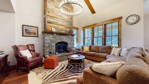 A cozy living room with a stone fireplace, leather armchair, and a large window with blinds. - Snowcreek VI The Lodges 1127 3 Suites, Spacious with Mountain Views, Private Garage and Washer Dryer by RedAwning (Mammoth Lakes)