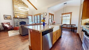 A spacious kitchen with a large island, wooden cabinets, a stone fireplace, and a dining area with a bench. - Snowcreek VI The Lodges 1127 3 Suites, Spacious with Mountain Views, Private Garage and Washer Dryer by RedAwning (Mammoth Lakes)
