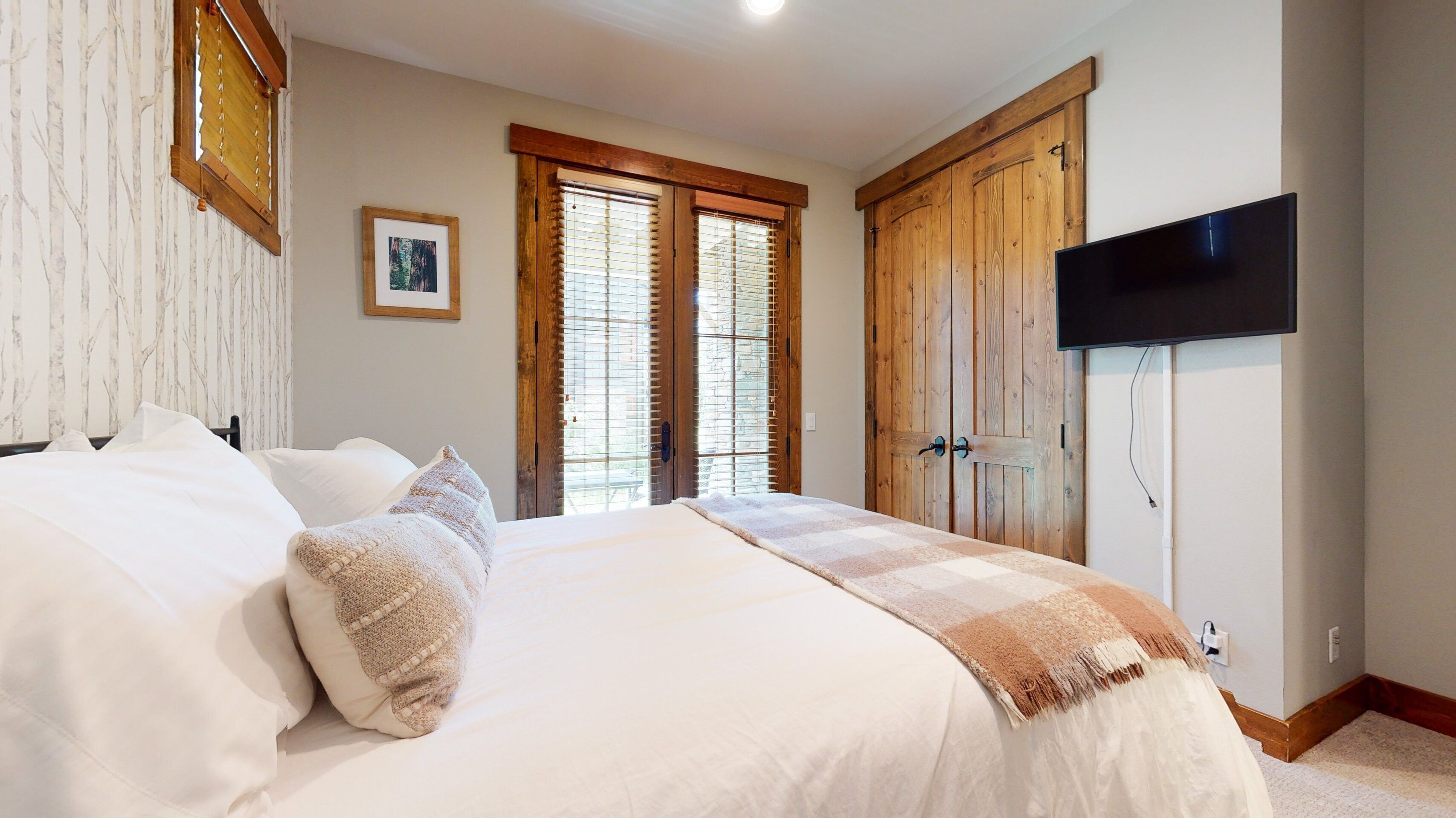 Een slaapkamer met een groot bed, een houten garderobe en een aan de muur bevestigde televisie.