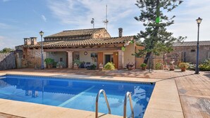 A swimming pool with metal ladders, surrounded by a patio with potted plants and a building with a tiled roof. - Hort de Sa Barrala, a small finca near Ses Covetes - Es Trenc beach (Ses Salines)