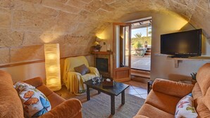A cozy living room with a stone ceiling, a flat-screen TV mounted on the wall, and a comfortable seating area with sofas and a coffee table. - Hort de Sa Barrala, a small finca near Ses Covetes - Es Trenc beach (Ses Salines)