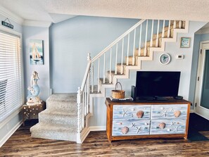 A staircase with white balusters, a television on a wooden stand, and a wall clock.