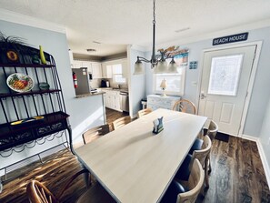 A modern kitchen with white cabinets, a dining area with a wooden table and chairs, and a sign reading "BEACH HOUSE". - Beach Property - Private Townhome w/ Balconies, 3 Bedrm 2 1/2 Bath, 2 Car Garage (Murrells Inlet)