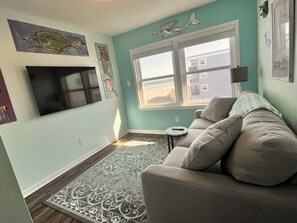 A living room with teal walls, a gray sofa, a patterned rug, and artwork on the walls. - Beach Property - Private Townhome w/ Balconies, 3 Bedrm 2 1/2 Bath, 2 Car Garage (Murrells Inlet)