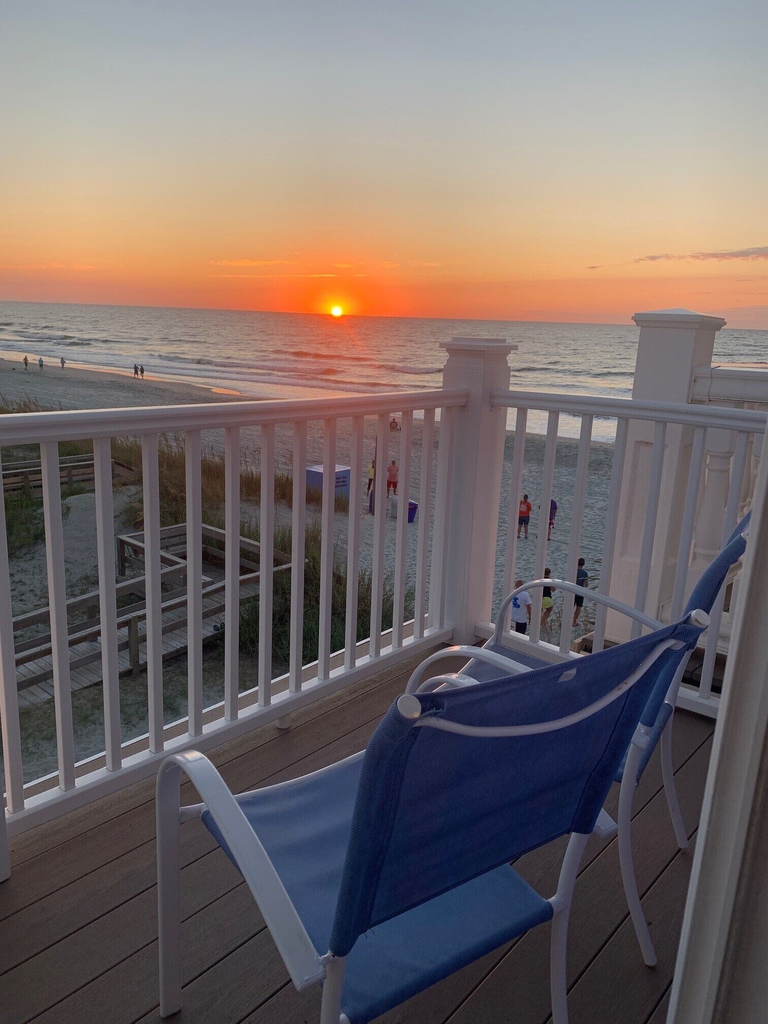 A deck with a view of the sunset over the ocean, featuring a railing and a blue chair.